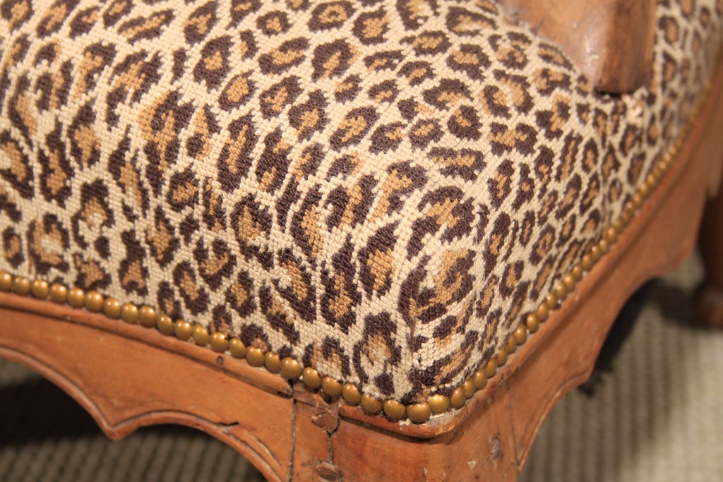 Lovely low-seating country French faded walnut Louis XV fireside chair with leopard tapestry covering.