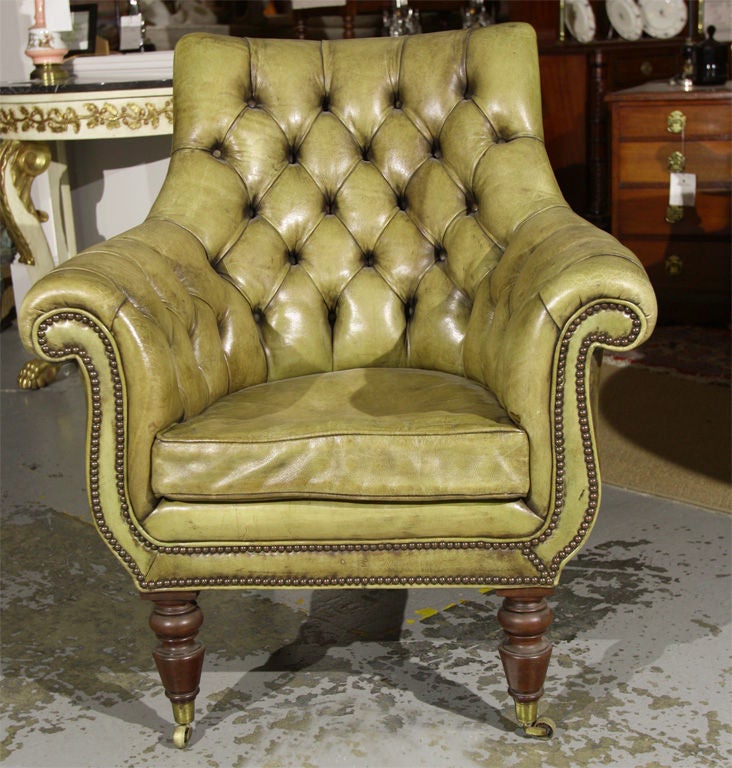 An English tufted green leather library chair with old restored leather and nailhead upholstery having turned tapering mahogany legs ending on brass casters.