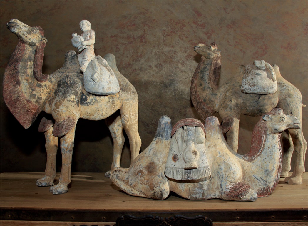 An exceptional grouping of three painted pottery camels.  Two modeled standing foursquare with heads raised, the third in recumbent position.  Each of the camels with detailed detachable saddlebags that are painted with red and white pigments and
