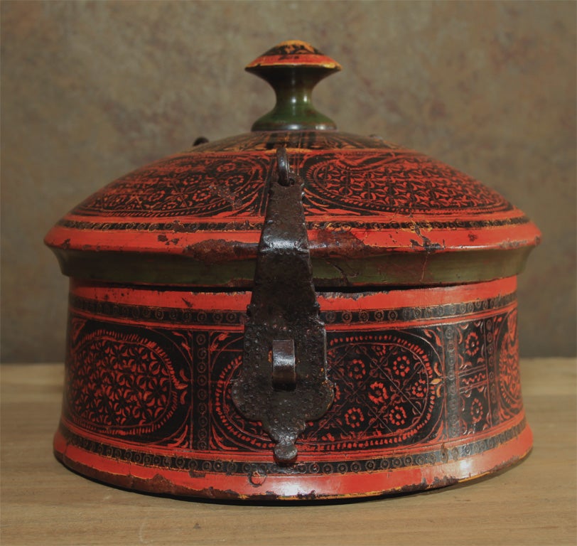 A fine example of a lidded lacquered box from the Hindu Kush area of Northern India. The straight sided box with a domed top and finial two wrought iron hinge strap offset to one side with latch on the other. Good over all red color with paisley
