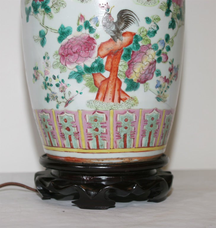 THE BALUSTER-FORM VASE DECORATED WITH PEONIES, BUTTERFLIES AND ROOSTERS PAINTED IN COLOR ENAMELS, RAISED ON A CARVED-WOOD BASE AND MOUNTED AS A LAMP.