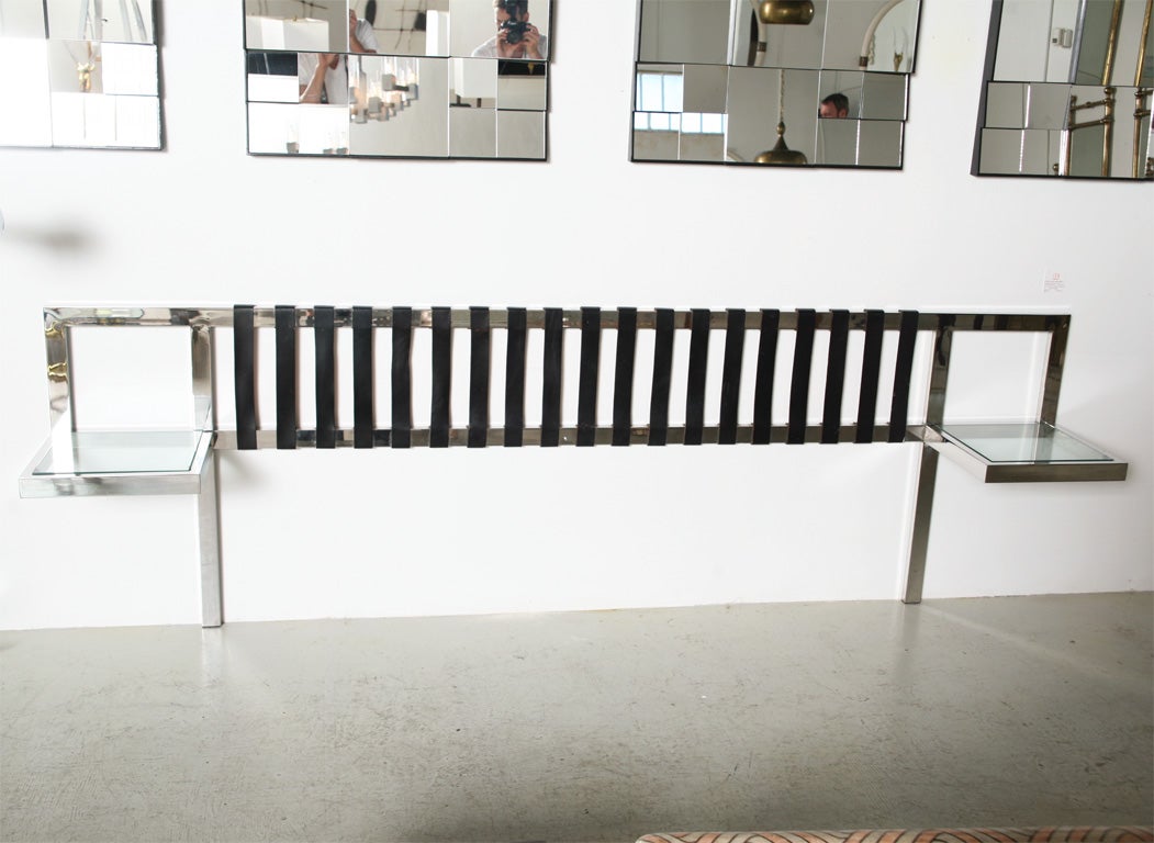 Long, low bold prismatic form in highly polished nickel. Thick glass inset tops define the night table/shelves. Black leather vertical straps stretched between the nickel bars form the actual headboard area. Finest construction.