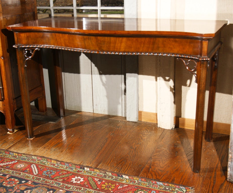 Georgian style, serpentine front mahogany serving table with gadroon carving to bottom of apron.  Rococo corner brackets to the chamfered legs complete the patrician appearance of this elegant table.