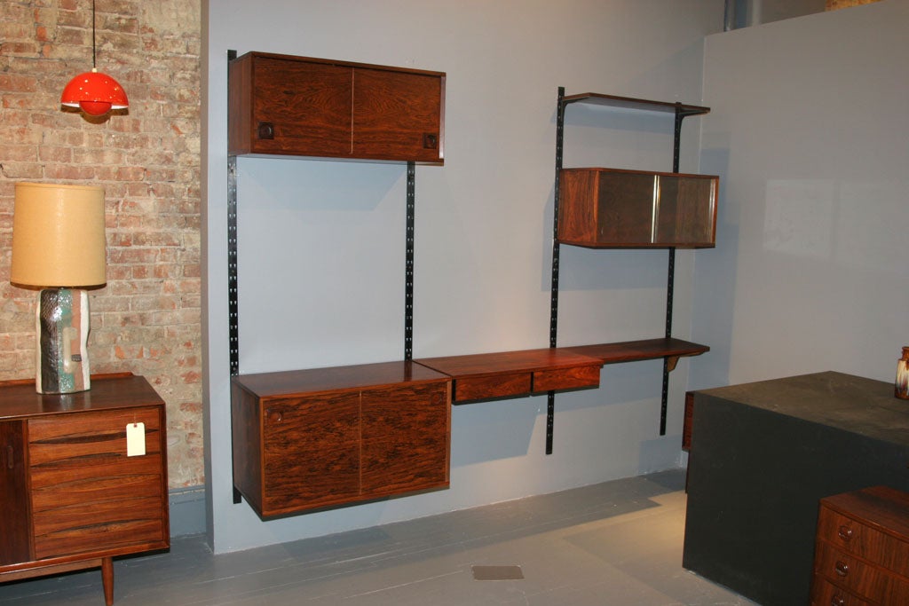 Modular 1960's Rosewood Wall Unit.  Features 3 cabinets with sliding doors, 4 shelves (2 not pictured), and a writing surface with drawers.  Each unit is height adjustable and is mounted on  4 vertical steel rods.
