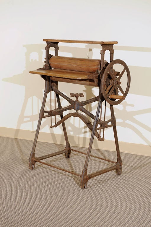 A fine working example of a hand mangle, used for squeezing water from wet garments and fabrics prior to hanging on a washing line. A cast iron stand supports two massive maple rollers with a beechwood shelf for feeding cloth in between. Iron leaf