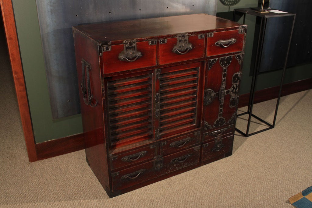 A Japanese shop chest, choba dansu, crafted entirely of sugi (cryptomeria) wood. The tansu with a deep brown-red semi-translucent lacquer finish. The chest with three drawers above a pair of sliding doors and tall hinged door, all above a group of