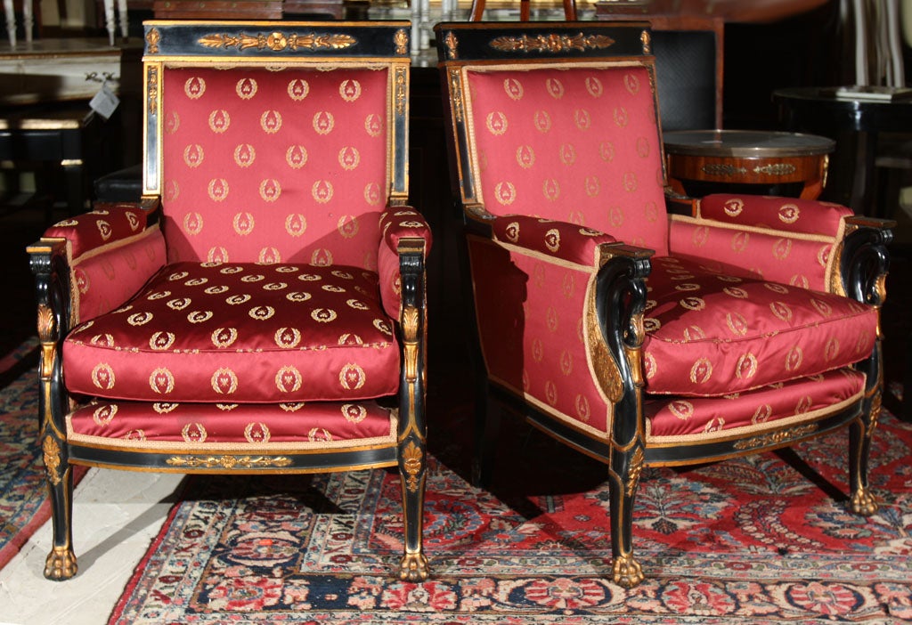 Pair of French empire style arm chairs, each ebonized and parcel-gilded with scrolled swan-head decorated arms, standing on hoof feet, upholstered in silk. Stamped Jansen