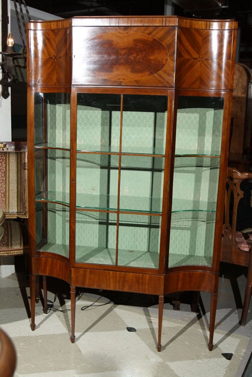 A very fine serpentine front mahogany & satinwood inlaid English curio cabinet, the paneled & curved glass doors with two glass shelves and silk-upholstered back splat, standing on tapering legs. The sides concave.