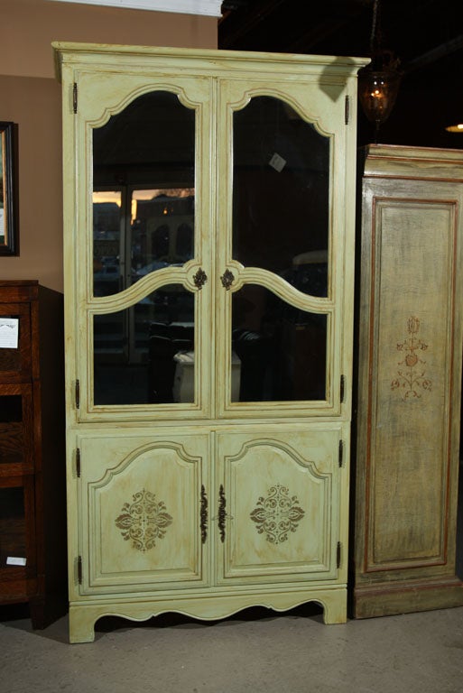 A pair of green distressed painted armoires by Baker, each with two glass doors over a two-door cabinet, standing on splayed bracket feet. Each bearing the Baker Furniture Company on the reverse. Oak interiors.