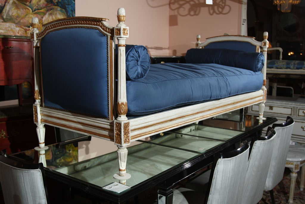 A fantastic painted and gilded daybed, circa 1930s in the style of Louis XVI, upholstered in blue cotton sateen with two bolster pillows, stamped Jansen. Seat height 19 1/2