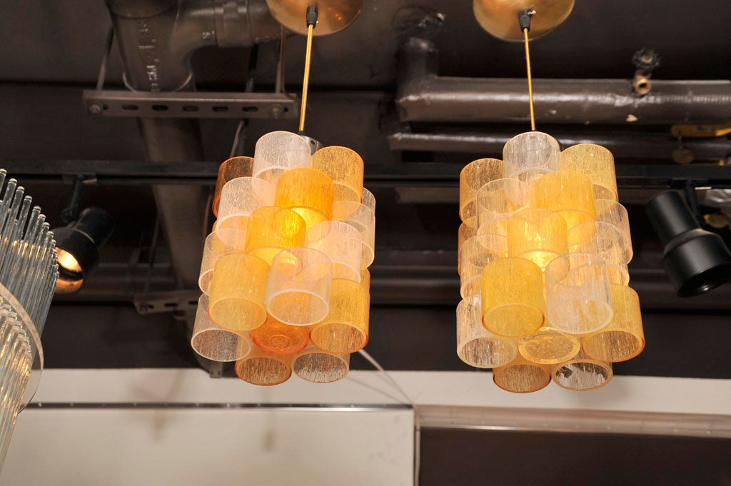 Hand blown murano glass cylinders<br />
in shades of amber and white glass<br />
with brushed brass and steel<br />
fittings.  Cord can be modified to<br />
hang at desired height. Can also<br />
be sold separate at $1,850 each.