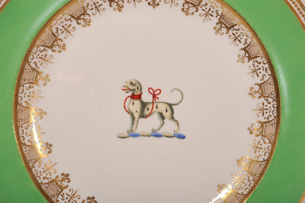 A group of a dozen Spode, apple green, armorial dinner plates feature in the center a stylized dog with a red rope forming a leash and collar.The dog is the emblem of faithfulness and guardianship. Dogs symbolize courage and vigilance. Around the