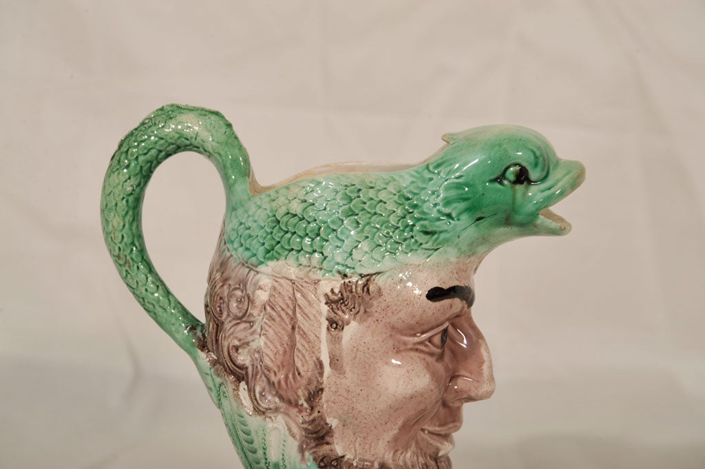 An 18th century creamware, dolphin head mask jug in the style of Ralph Wood with the dolphin and the foot lightly covered in a green translucent glaze and the satyr's face covered in a manganese wash (See Captain R.K. Rice, 