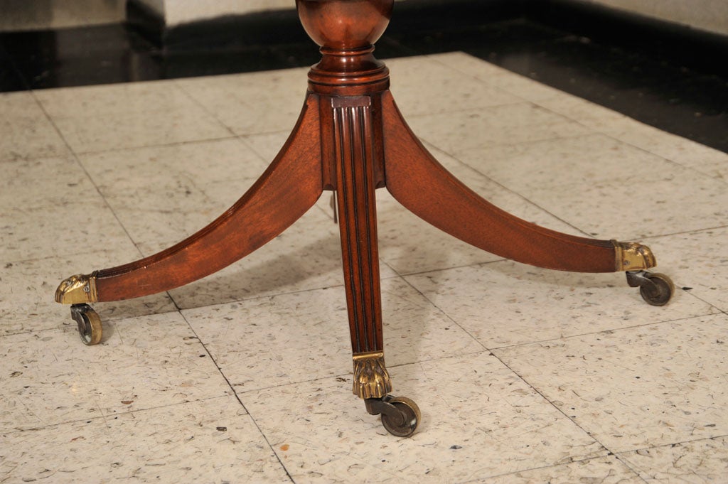 Vintage Revolving Library/End Table with Richly Patinated Inset Leather Top Above Four Cupboards Separated by Leather Book Spines; All Supported by Curved Reeded Legs on Brass Casters.  England, Early 20th Century.<br />
<br />
30 inches diameter