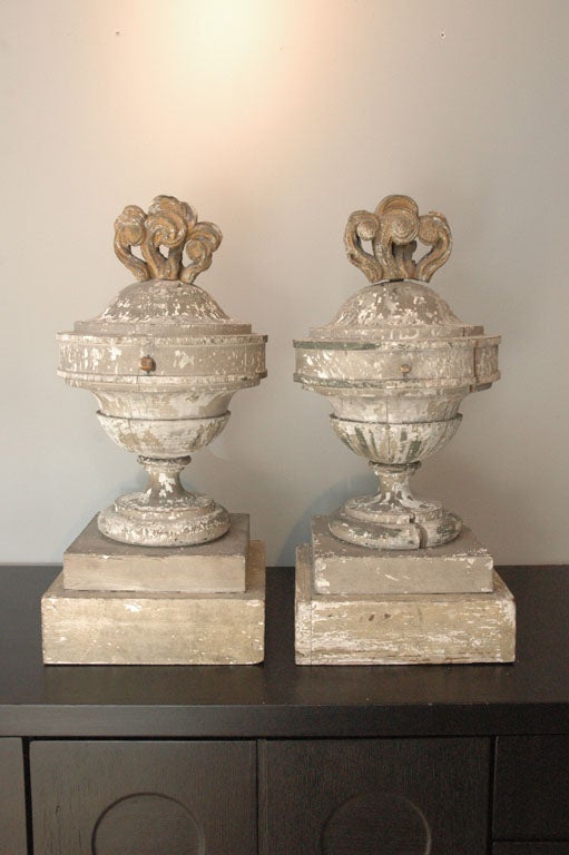 A very fine pair of wooden garden urns with sharp classical details including a gilt wooden fire finial at the top. The finish is gray with chipping white paint which gives them amazing patina and character.