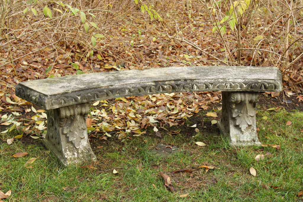 A curved composition stone bench with egg and dart edging on supports with foliate decoration.