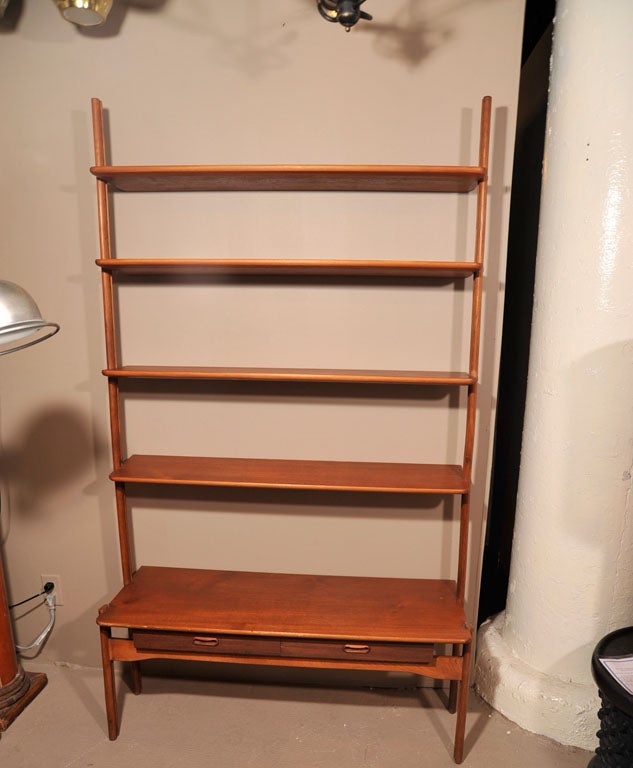 Teak bookcase/cabinet wall unit. Denmark, circa 1950.

Features four adjustable, upper shelves and a fifth lower shelf over two drawers. Brass bracket secures cabinet to wall.

Measures 72