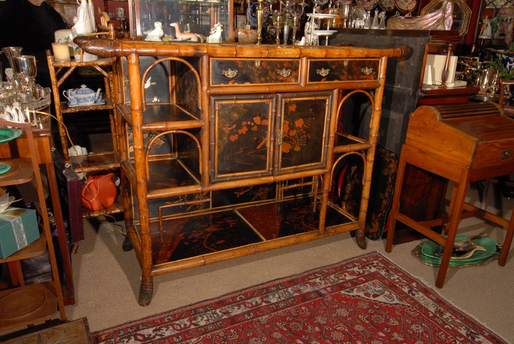 An English bamboo console cabinet from the Aesthetic Movement Period featuring a beautiful lacquered top, sides and cabinet doors. The framework featuring bamboo with the root ends showing as ornamental decoration on the top and feet. 
The console