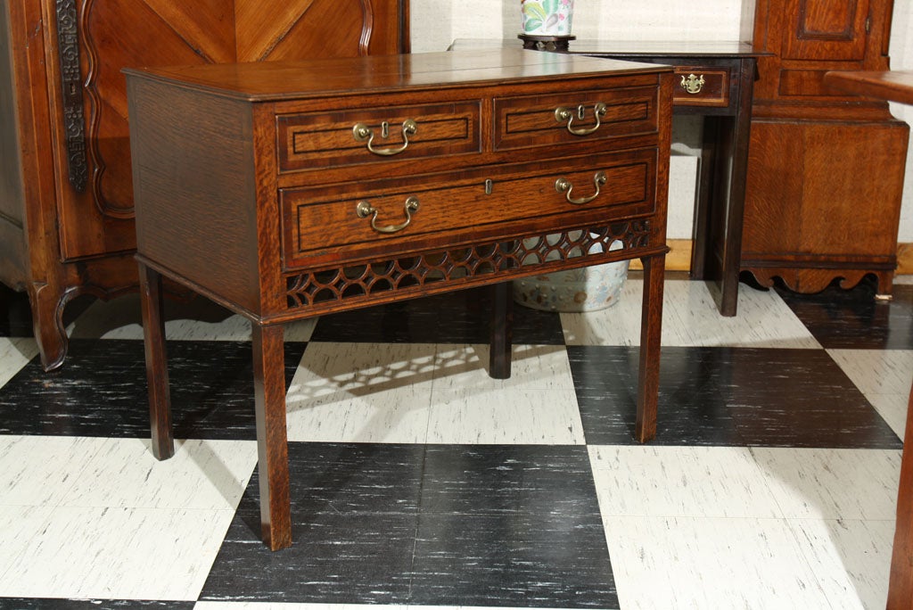 Irish, three-drawer lowboy in quartersawn oak with ebony and fruitwood inlays and a unique open fret apron. Top and drawers are cross banded in mahogany. Brass bail pulls and escutcheons highlight the dovetailed drawers while a thin moulding defines