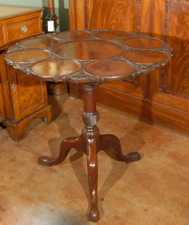 An English supper or tea table of mahogany featuring a gadroon-edge round revolving top and place-settings for serving plates, over a birdcage support featuring four columns of turned wood with brass hardware, standing on a tripod pedestal column on