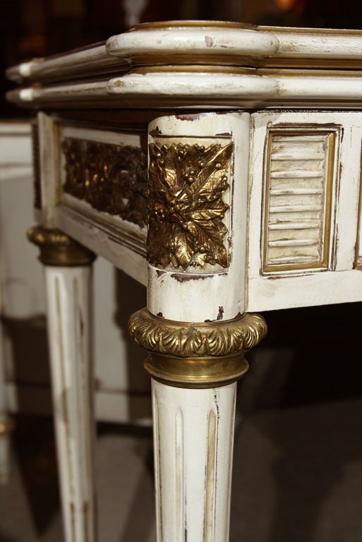 An elegant white painted and parcel-gilded console table, the rectangular top opens to a wider writing surface, over a frieze of two narrow drawers with bronze scroll work all around, supported by circular fluted legs ending in capped feet. Stamped
