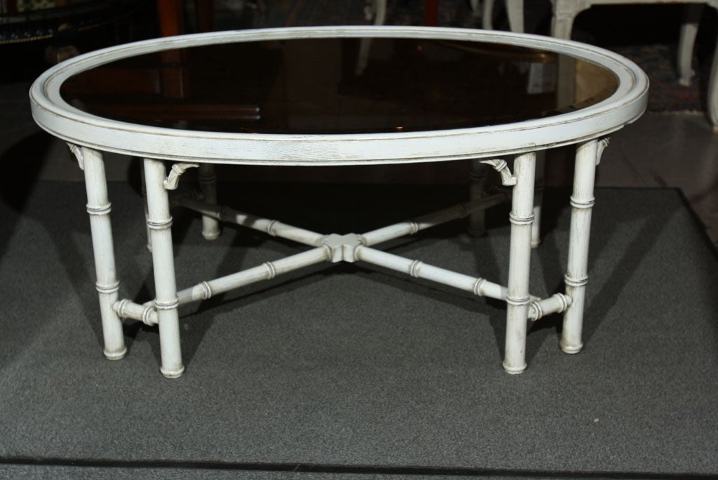 An oval coffee table, white painted with verre églomisé glass top, the faux bamboo legs joint by X-stretcher, Jansen.
