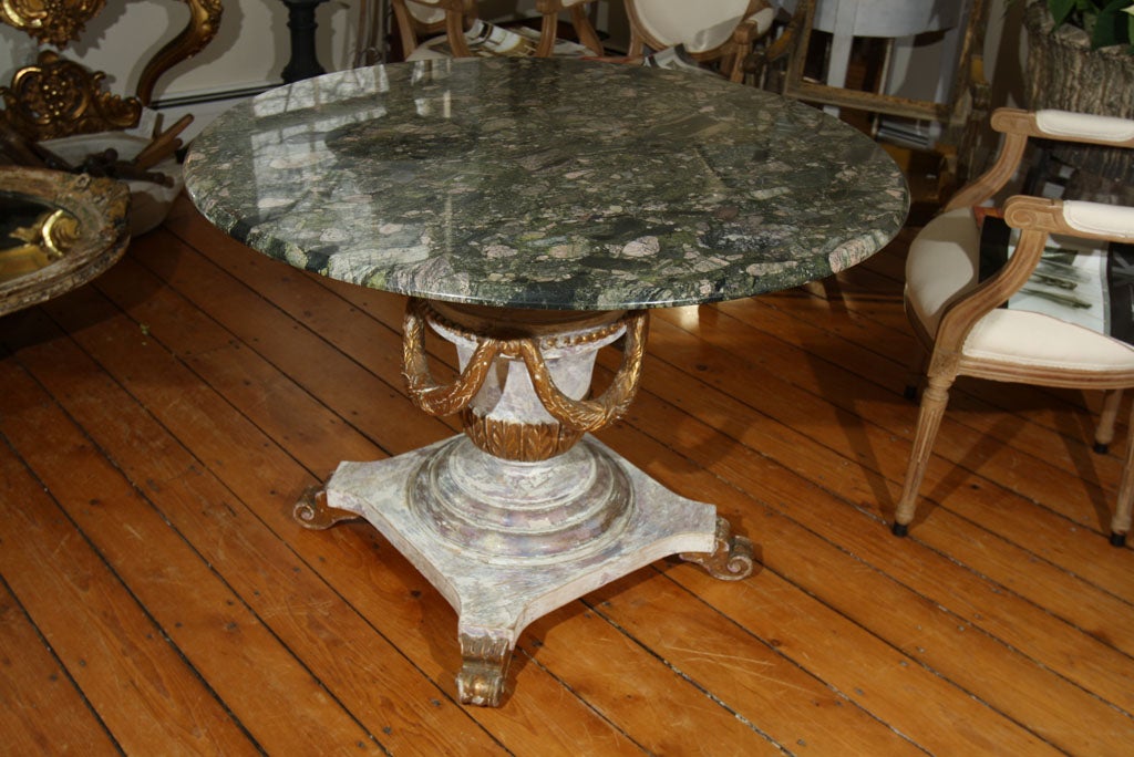 This table is over the top! The wooden base is beautifully painted with undertones of purple, grey and pink and a surface wash of translucent white. The base is carved in an urn shape with gilded anthemion leaves and beaded rim from which four