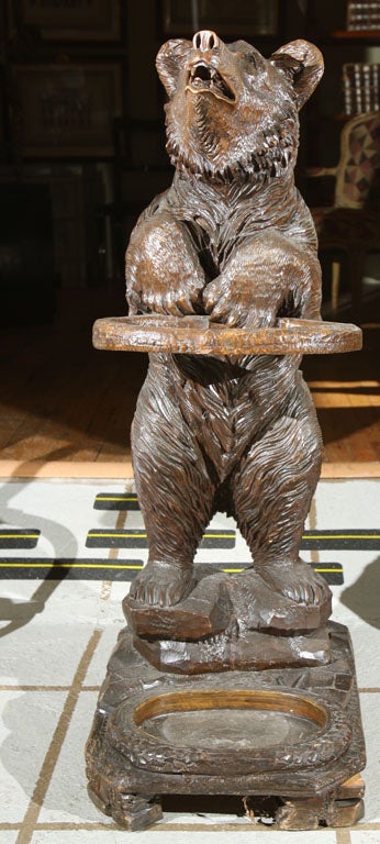 Carved and painted wood standing bear on a rocky base holding a ring support. The base with a well.