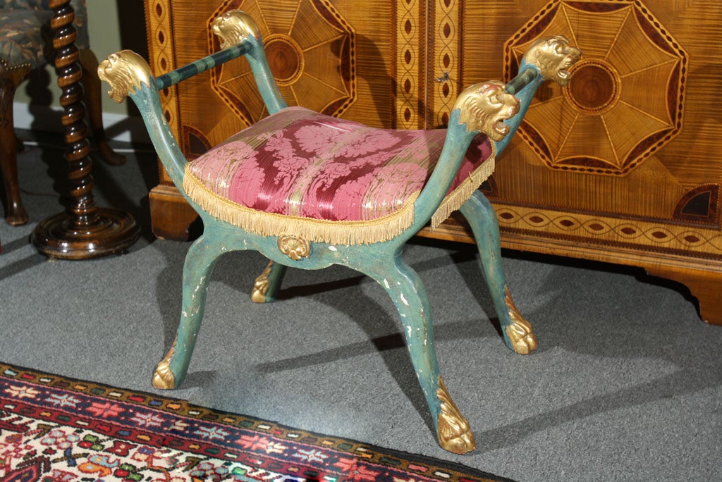 Wood in green paint and parcel gilt with lion's head terminals and paw and acanthus leaf feet. Shell motifs on the apron, the stretchers with painted blue stripes. A damask upholstered seat.