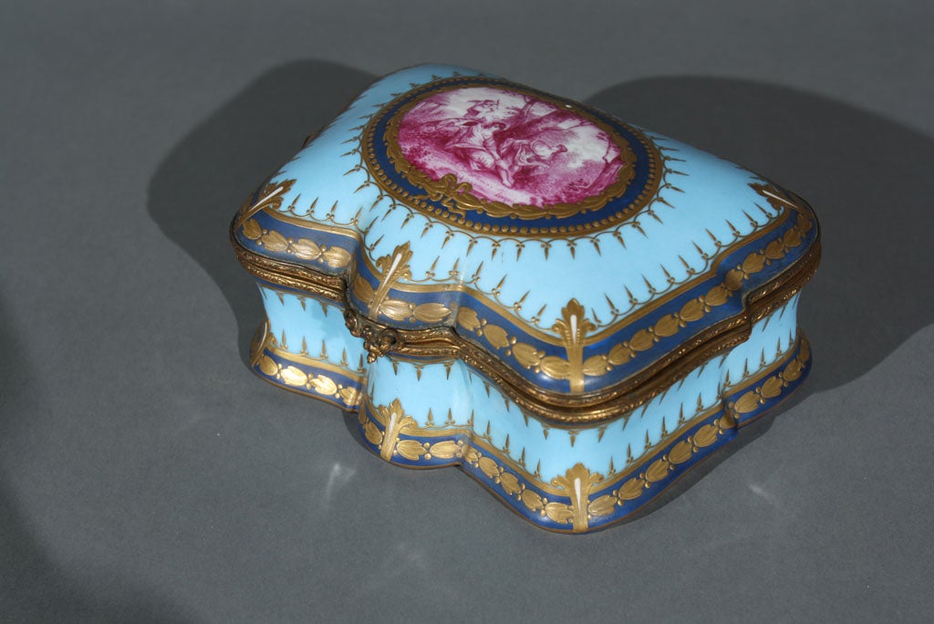 A late 19th century cartouche shaped painted and parcel gilt Sevres box signed Lauque bearing the interlaced L's mark.  The top is decorated with an oval fuschia colored classical scene with the interior decorated with flowers.