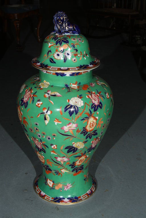 An ironstone green ground vase with with cover topped by a lion finial with floral decoration and gilding.