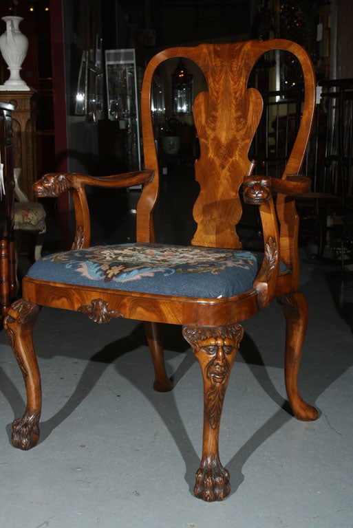 A Georgian style carved walnut open armchair with grotesque carvings to the arms and knees with a drop-in needlepoint seat ending on on furry lion's paw feet.