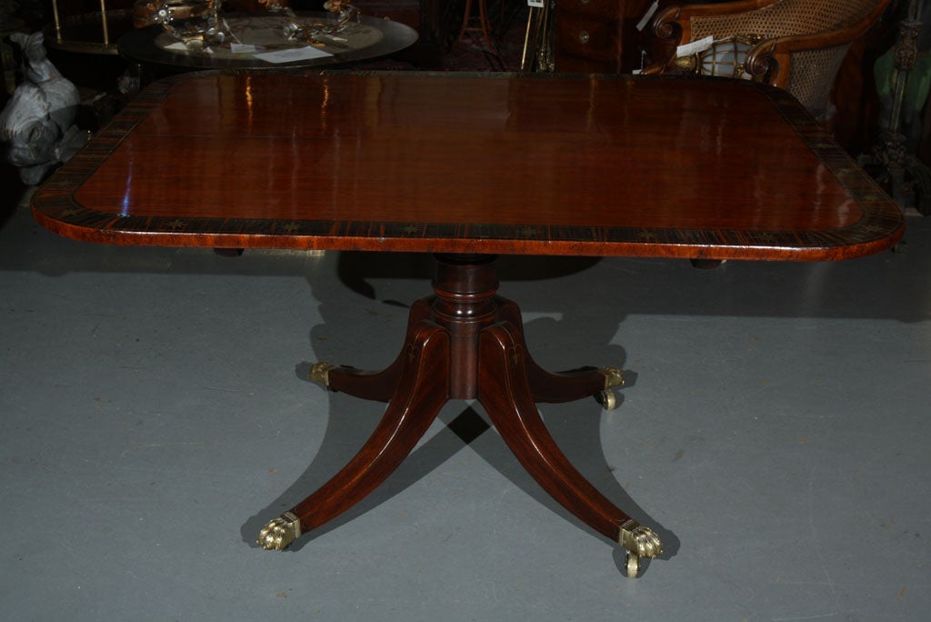 A Regency period mahogany breakfast table with a wonderful calamander wood and brass inlaid banded top raised on brass inlaid splayed legs with lion's paw feet ending on casters.