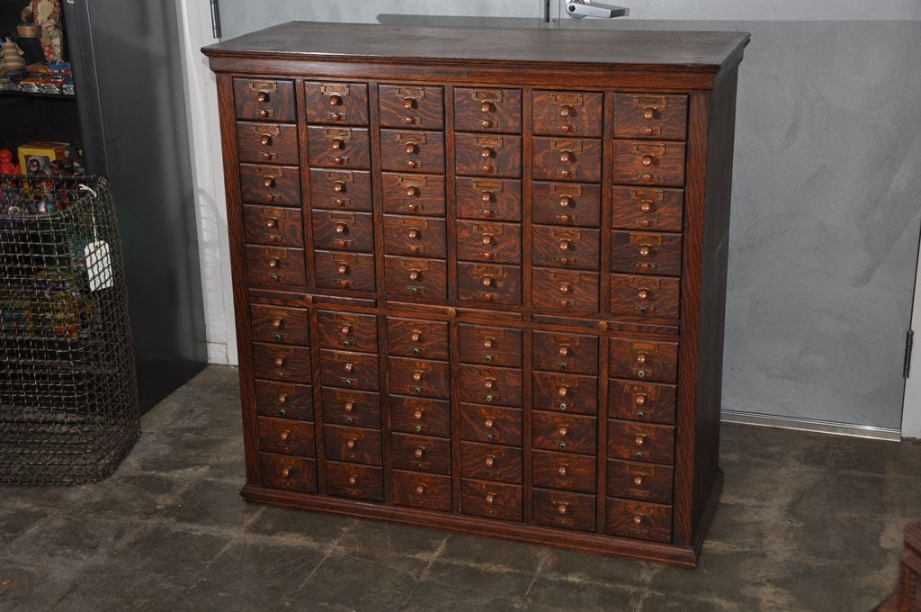 This American library filing cabinet, circa 1908, has 60 drawers with associated name card, handles and adjusting elements. The cabinet is solid oak, very heavy, and has three slides at the mid section. Adjusting elements have been remove from