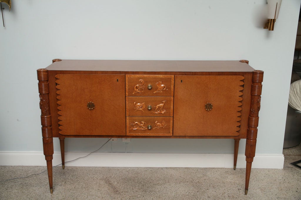 The rectangular top with rounded edges above three central drawers with animal motif flanked by two doors, the legs reeded and tapering with similar animal motif.