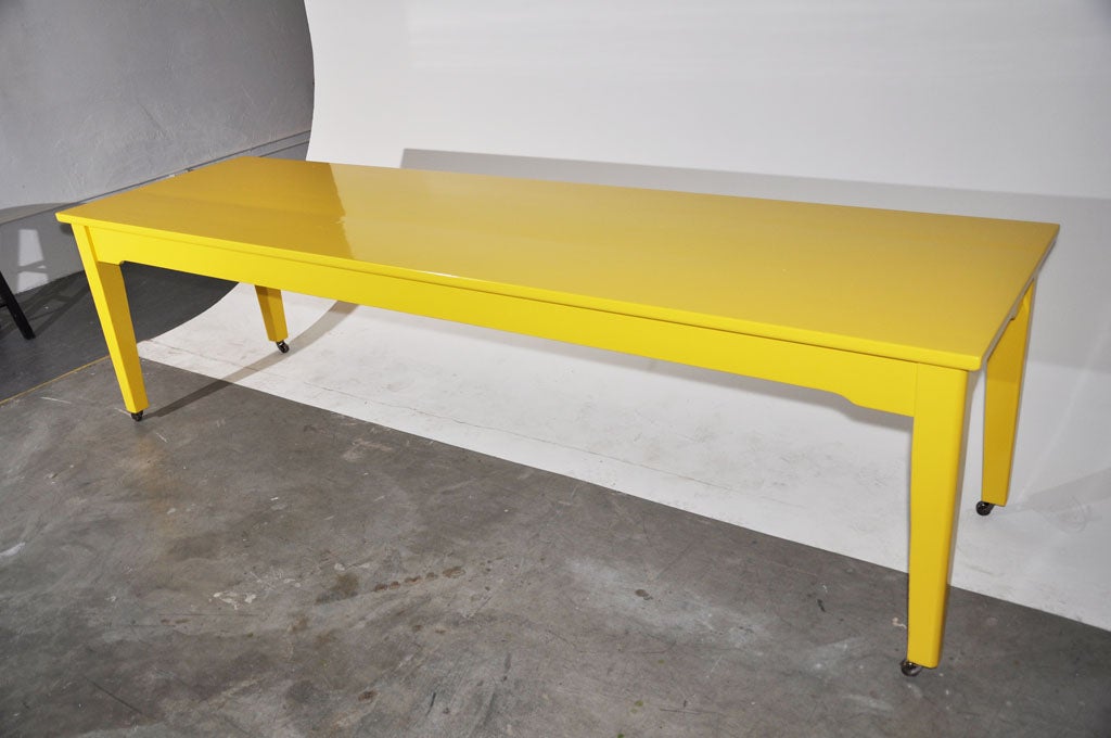 Versatile American made school table newly painted in a sunny schoolbus yellow lacquer, supported by sturdy solid wood legs with a slight arch detail on the frame. New brass caster wheels have been added for additional versatility. Custom sizes are