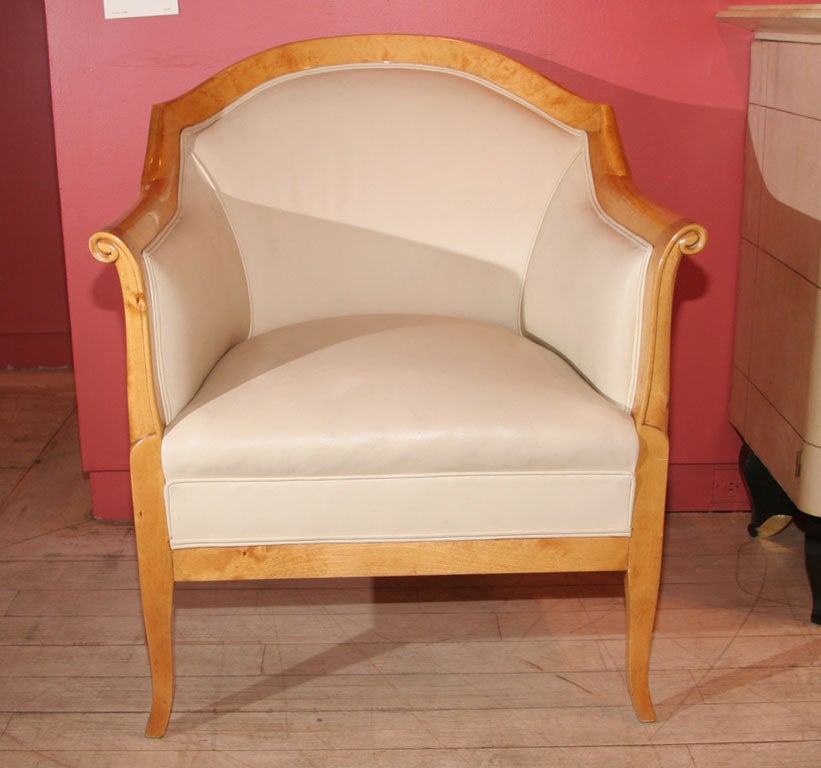 The upholstered barrel back flanked by carved scroll arms centering an attached seat, all raised on sabre legs.