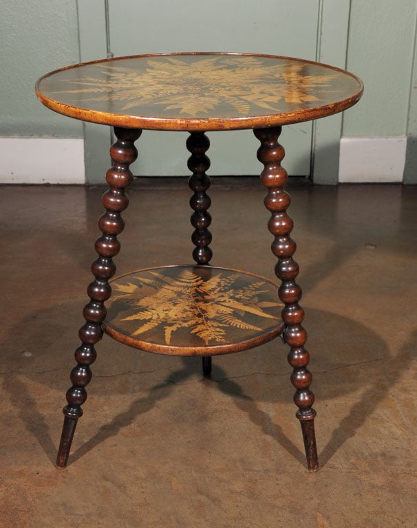 An unusual find - a Fernware table from Mauchline, Scotland featuring two tiers with a decorative design of ferns upon each top adjoined to a bobbin-spool leg tripod support.<br />
<br />
From the book, Mauchline Ware by John Baker:<br />
<br