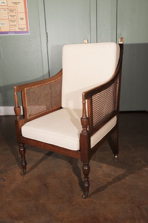 A classic library armchair of Cuban mahogany from the Edwardian-era, with caned sides and back featuring Modern style drop-in back and seat cushions, on rolling brass casters.