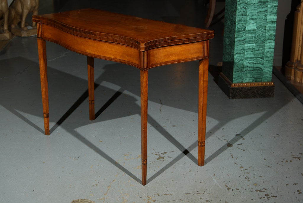 A late 18th century English satinwood card table with a serpentine front and mahogany banding.  In an extra large size and an interesting detail on the tapered legs.