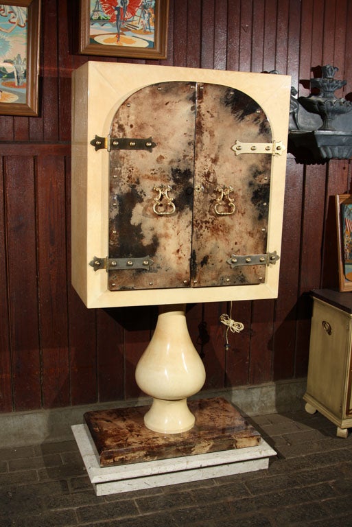 Two door goat skin parchment bar cabinet on a pedestal base by Aldo Tura. The fanciful metal hardware is gilded.  The interior is mirrored with two glass shelves and illuminates when opened. Base is 32
