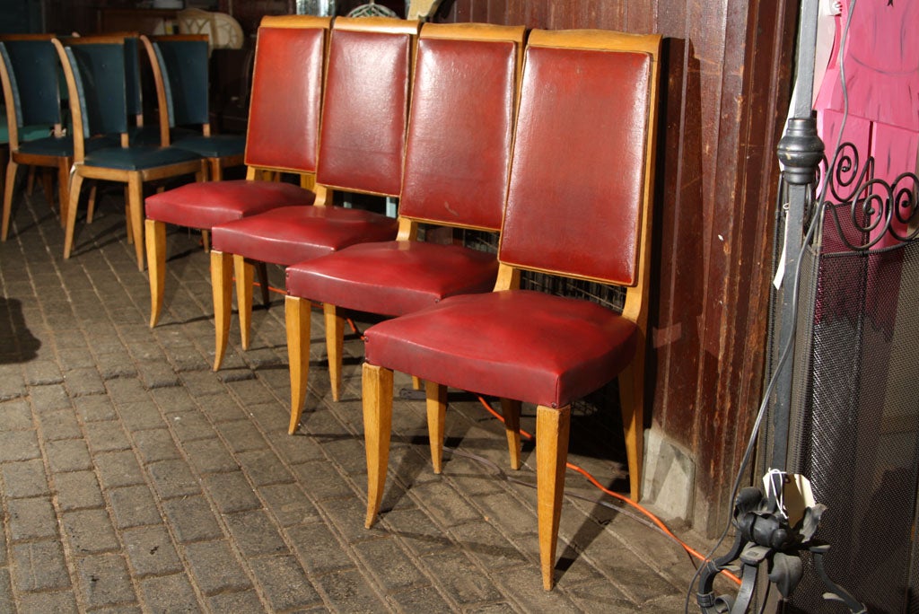 Set of four high back French dining chairs upholstered in red oil cloth with medium wood colored frames. Wood frames are sturdy. Seat springs need to be retied.