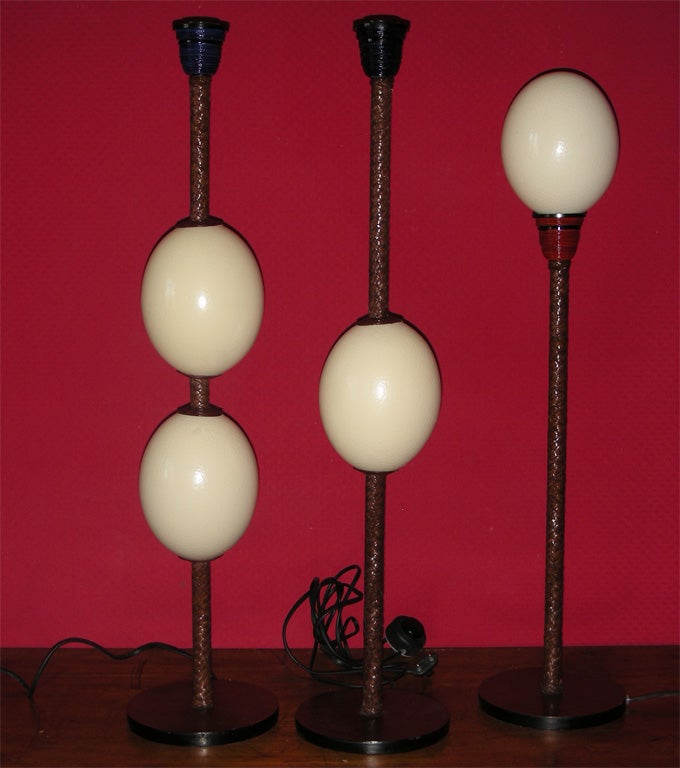 Three 1990s lamps by Frédérique Lombard Morel with shafts clad in leather and ostrich eggs inserted on their length. Smallest lamp height 70 cm., diameter 16 cm.