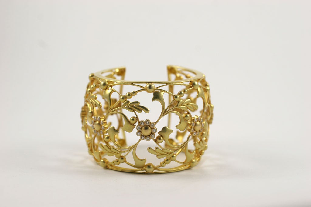 An 18kt yellow gold and diamond cuff. The cuff is composed of 18kt yellow gold vines, leaves and flowers. Each flower is surrounded by a border of diamonds.