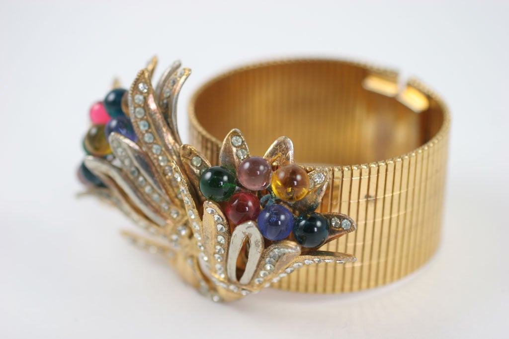Flexible wide band bracelet decorated with a large rhinestone and glass bead adorned floral cluster.