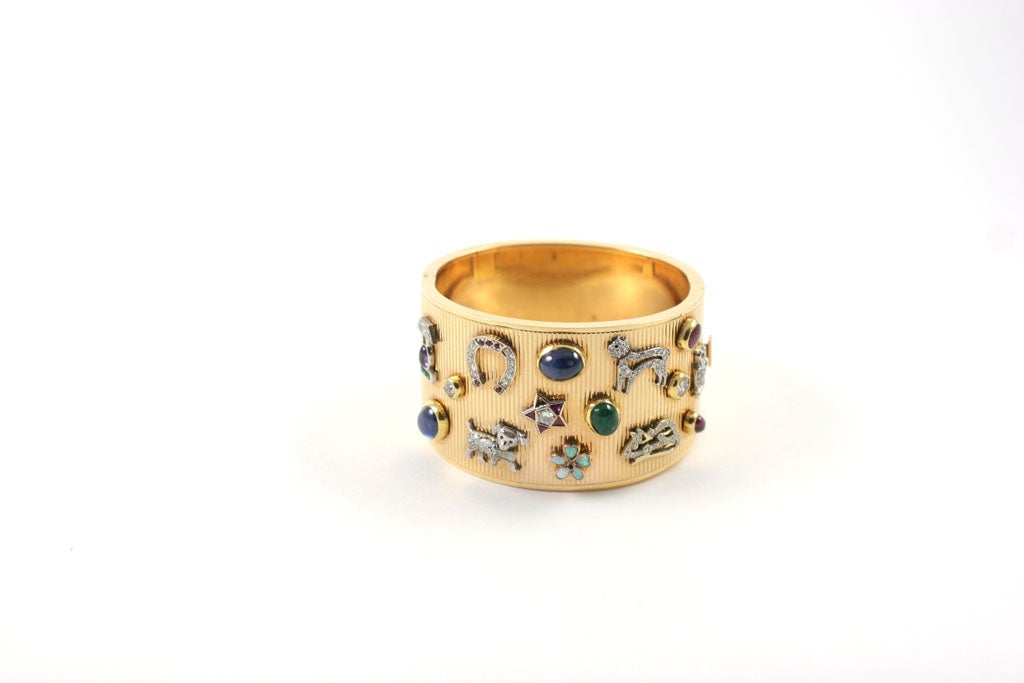 The 14K Gold reeded cuff is studded with 15 period Art Deco charms including a platinum, ruby and diamond owl, a diamond mouse, a diamond cat and dog, a diamond horseshoe, a ruby and diamond star, an opal and sapphire flower, an amthyst, emerald and