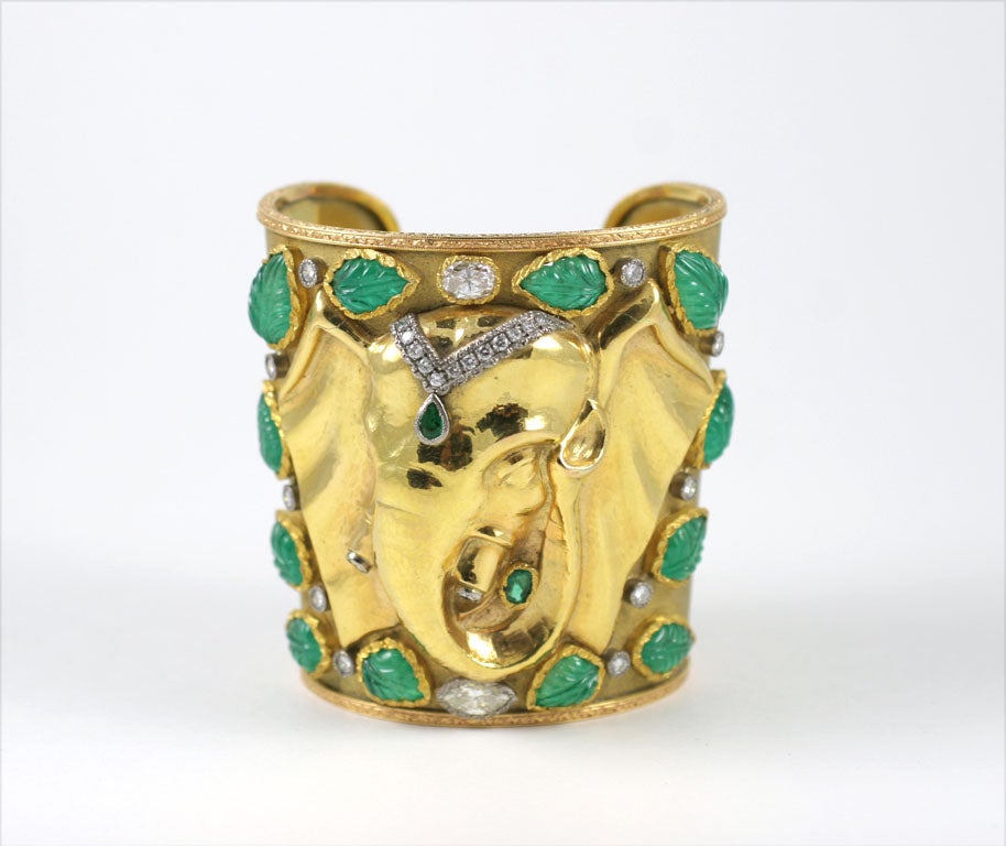 Tapered cuff decorated with an elephant head, the forehead decorated with a pear-shaped emerald pendant on a chain set with brilliant-cut diamonds, the tusks accented with brilliant-cut diamonds, the bangle is encrusted with carved leaf-shaped
