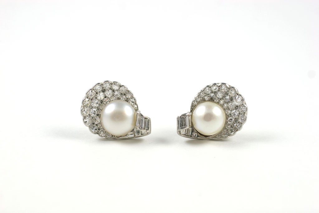 Each shell-shaped earring set with a natural pearl measuring 10.8mm and 11.5mm respectively and decorated with single-cut and baguette diamonds.