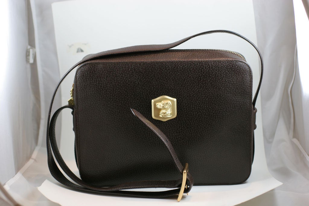 Brown leather Kieselstein-Cord camera shoulder bag with dog plaque on front and crescent moon and star pull on zipper. Date on hardware is 1985. Bag is lined in brown fabric and has a zipper compartment. Shoulder strap is adjustable. Total length of