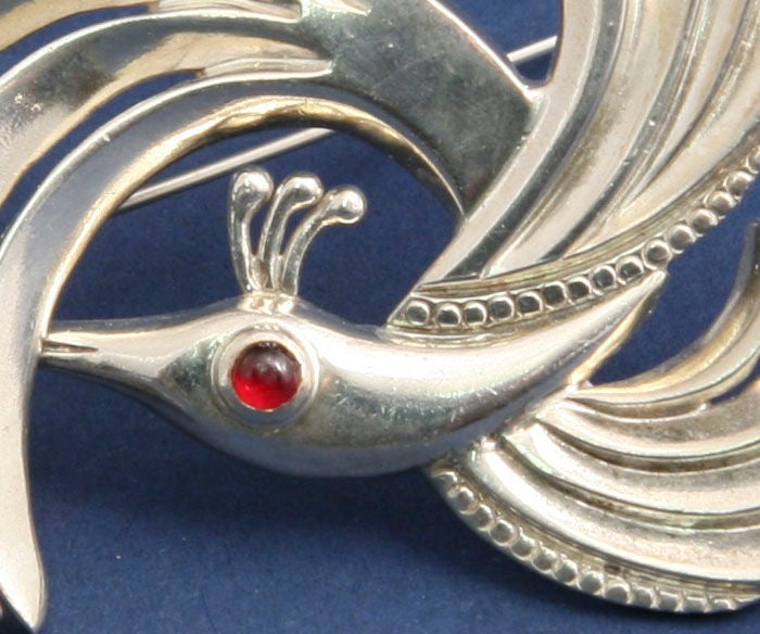 A swirling mythological bird with a garnet eye by Taxco master jeweler, Antonio Pineda (1919-2009).  Hallmarked on the reverse with Antonio's crown mark, the eagle 58 mark, which was the Mexican government's mark guaranteeing sterling content and